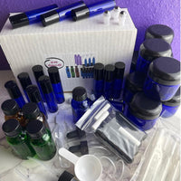 Thumbnail for A bulk set of cosmetic and fragrance-making supplies, including multiple blue glass bottles, amber glass bottles, black-lidded jars, small roll-on vials, clear plastic tubes, and a white box labeled '31 PC Cosmetics'.