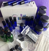 Thumbnail for A fragrance oil kit with multiple blue glass bottles, green glass bottles, white and black atomizers, a white box labeled 'Sine Olfactory', and various clear plastic transfer bags, pipettes, and a white scoop, arranged on a white marble surface against a purple background.
